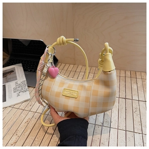 Close-up of yellow checkered crescent bag with leather brand tag and heart charm accessory