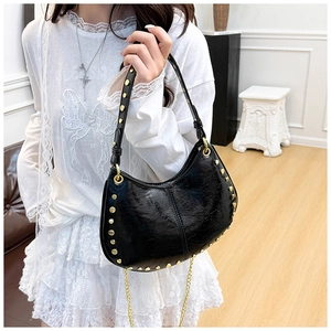Detail of black leather crescent bag featuring gold stud rivets and chain shoulder strap