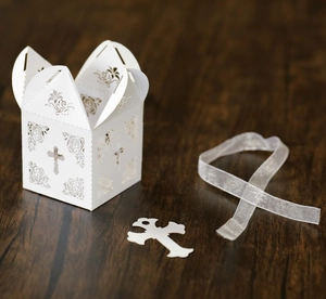Detail of white laser-cut candy box with cross pattern and elegant ribbon on wood table