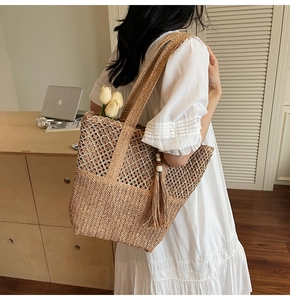 Detail of a khaki woven straw tote bag with diamond cutout patterns and fringe tassel