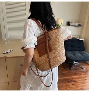 Close-up of a woven straw shoulder bag with dark brown leather pocket on the back