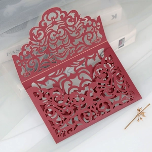 Detail of burgundy laser-cut wedding invitation with intricate floral scroll patterns