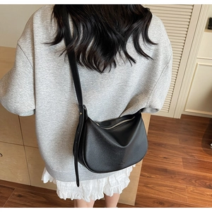 Detail of black lychee grain leather crossbody dumpling bag with adjustable strap on model