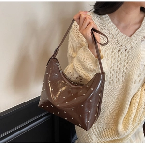 Brown glossy leather hobo bag with silver rivets worn by a model in a casual outfit