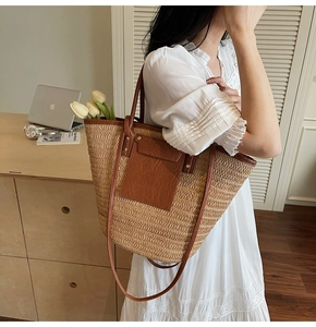 Detailed view of the large woven straw tote bag with brown leather handles and pocket
