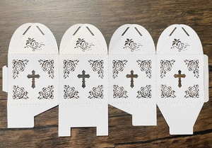 Flat lay of laser-cut white wedding favor box with cross and rose hollow pattern