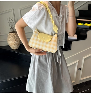 Detail of light yellow plaid shoulder bag with woven strap and logo on the flap