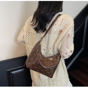 Brown patent leather hobo bag with silver rivets shown on shoulder by model