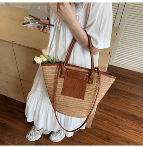 Detailed close-up of a woven straw tote bag featuring brown leather trim and pocket