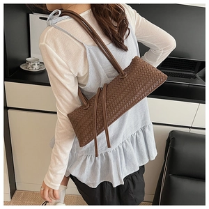Detail of dark brown woven baguette bag featuring long tassels and cross-weave texture