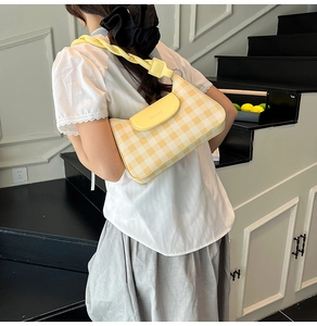 Detail of yellow and beige checkered shoulder bag with chic twisted strap and metal logo