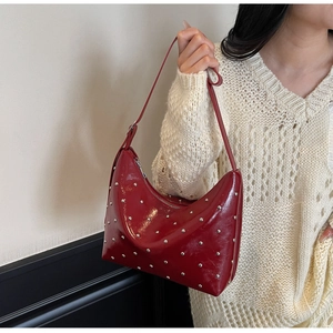 Detailed shot of red high-gloss crescent bag with silver rivet studs on textured sweater