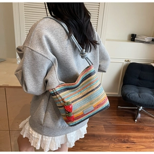 Détail du sac seau tissé à rayures colorées avec breloques fraises et bandoulière nouée