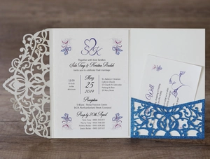 Detailed laser-cut cream wedding invitation set with glitter pocket on wooden background