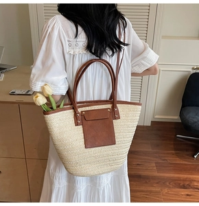 Straw tote bag with brown leather handles worn by model in a cozy indoor setting