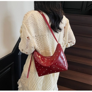 Red leather crescent shoulder bag with silver stud details shown on a model