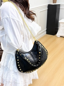 Black crescent shoulder bag with golden rivets and chain strap in a minimal setting