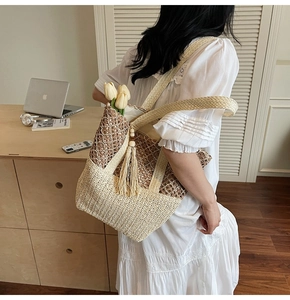 Detail of a large straw tote bag featuring contrast colors, tassel decor, and shoulder strap
