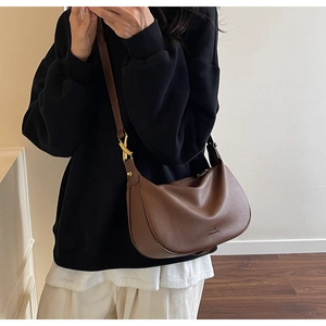 Detail of a dark brown pebble leather hobo bag featuring gold X-shaped metal hardware