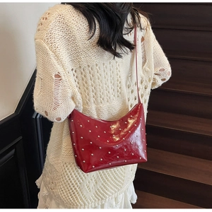 Detail of red glossy crescent bag featuring silver studs and slim shoulder strap on model