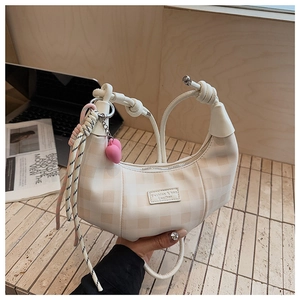 Detail of beige crescent bag featuring checkerboard texture and decorative heart charms