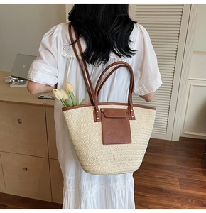 Detail of hand-woven straw tote bag with brown leather handles and decorative pocket