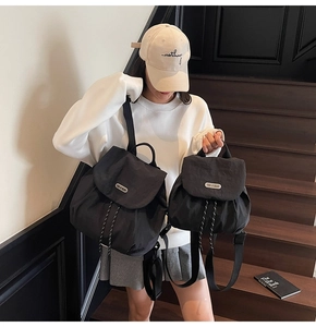 Size comparison of two black nylon backpacks with flap closure and metal logo on stairs