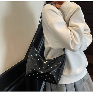 Fashionable black leather hobo bag with silver studs worn by a model in a minimal interior