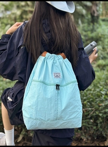 Detailed back view of a sky blue drawstring backpack with nylon texture in nature