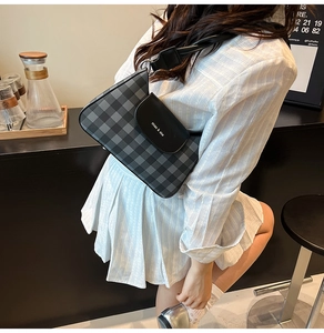 Close-up of black and grey plaid crossbody bag with leather flap and wide shoulder strap