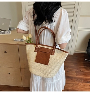 Detail of a large straw tote bag with brown leather pocket in a cozy home setting