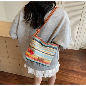 Détail du sac tissé aux rayures arc-en-ciel avec breloques fraises et bandoulière en cuir