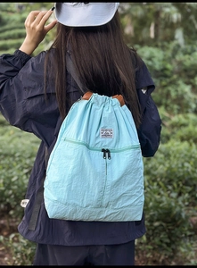 Outdoor view of a blue drawstring backpack with front zipper pocket and adjustable straps