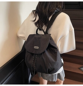 Close-up of black nylon backpack featuring flap cover with branded nameplate and drawstring