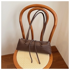Close-up of dark brown woven leather baguette bag with silver zipper on a vintage wooden chair