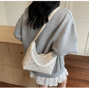 Detailed view of a white crescent shoulder bag with metallic silver rivets in daily use