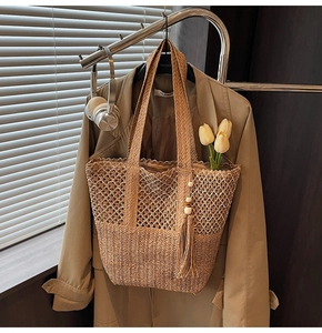 Detailed close-up of straw woven tote bag with tassel charm and textured knit pattern