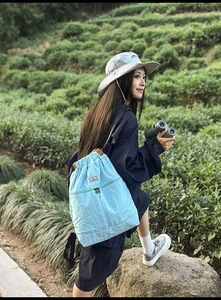 Detail of light blue drawstring backpack showing textured fabric in outdoor nature setting