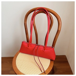 Detail of red woven leather shoulder bag with long straps and tassel zipper on wooden chair