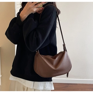 Brown leather crescent shoulder bag with adjustable strap worn by a model in a cozy room