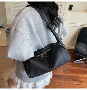 Dettaglio borsa a bauletto in pelle litchi nera con doppia tracolla e zip argento