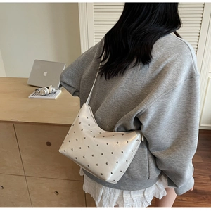 Detailed view of a white crescent hobo bag with metal rivets worn by a model