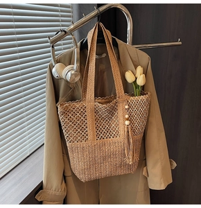 Detail of hand-woven straw tote bag featuring tassel charm and boho mesh pattern