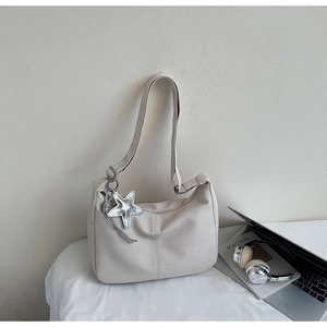 Detail view of cream tote bag with fine texture and silver star pendant accessory