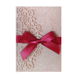 Close-up of laser cut glitter invitation card with red satin bow detail