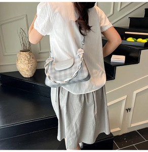 Silver checkered crossbody bag with woven decorative strap worn by model against wall