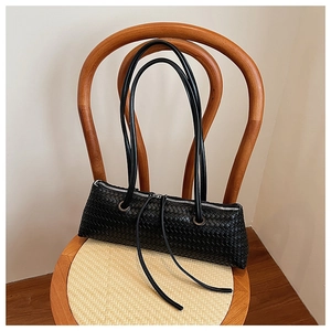 Close-up of black woven leather shoulder bag with fine intrecciato weave on a wooden chair