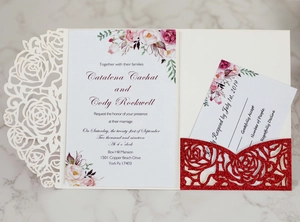 Macro shot of laser-cut rose wedding invitation set with red glitter pocket on marble surface