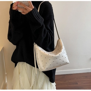 Close-up of cream Hobo shoulder bag with silver studs worn across the body