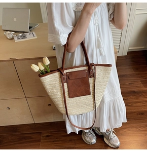 Detail of straw woven tote with brown leather pockets and rivets in a lifestyle setting